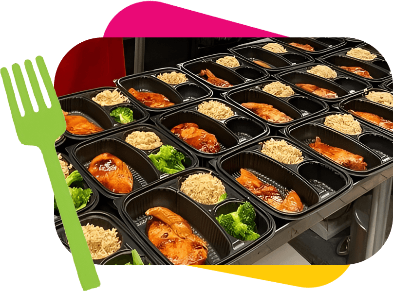 A row of black plastic meal trays containing portions of chicken, rice, and broccoli is neatly arranged on a metallic surface. A green fork graphic is positioned on the left side of the image.