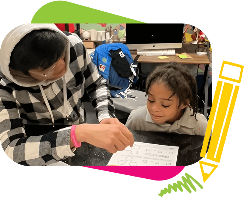 A person is helping a young child with a worksheet at a table. There is a computer and various items in the background. A pencil graphic decorates the corner of the image.