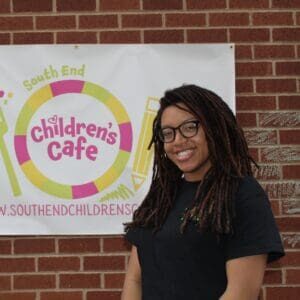 Smiling person in front of children's cafe banner.